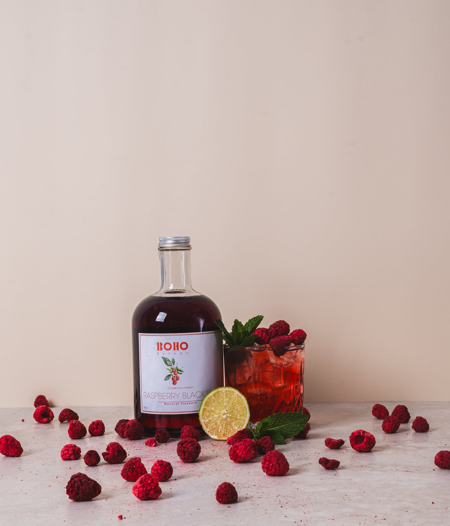 Fles BOHO framboos zwarte thee siroop met daarnaast een mooi gegarneerd glas homemade iced tea – fruitige en verfrissende creatie