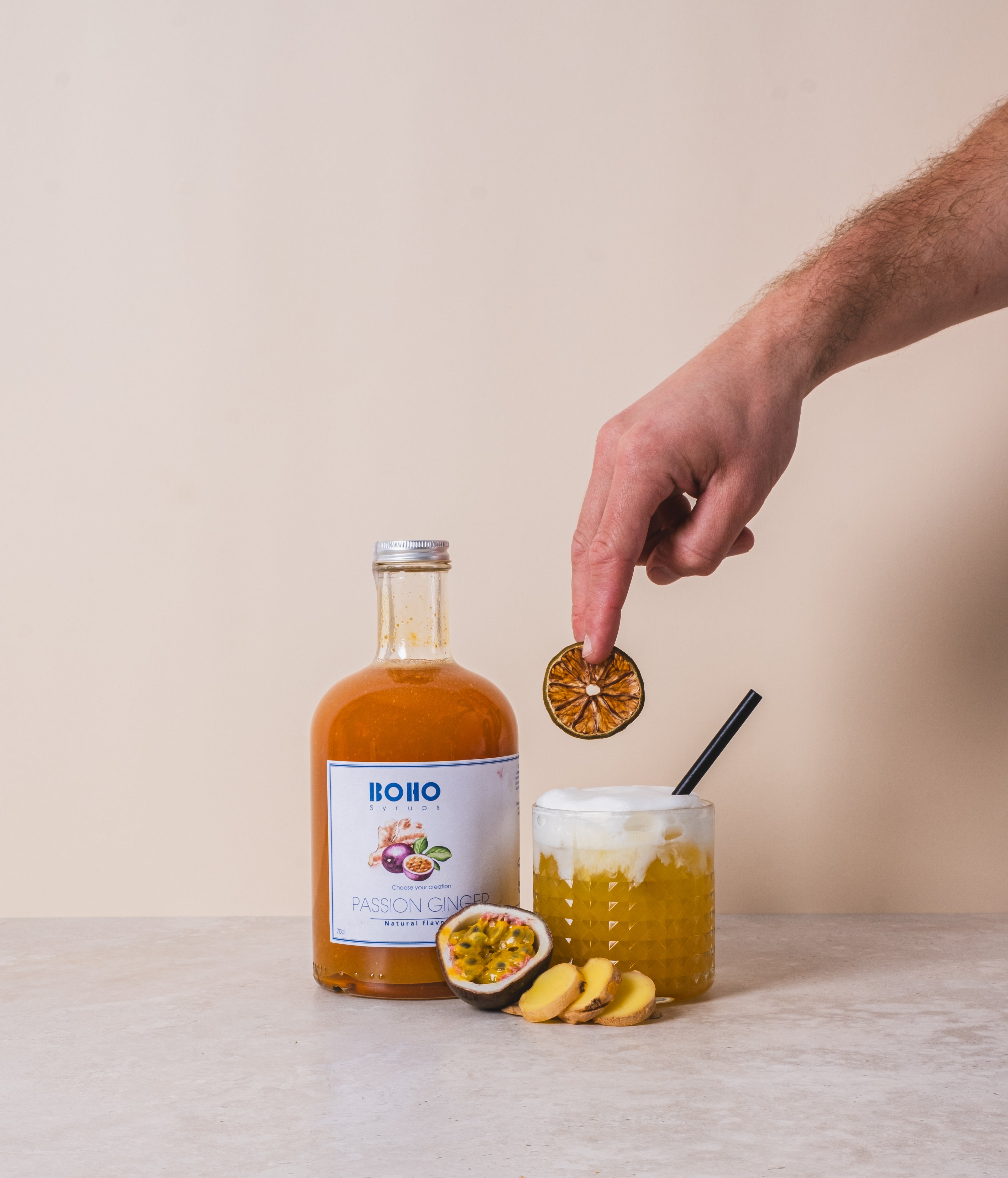 Fles BOHO passievrucht gember siroop met daarnaast een glas mocktail dat met de hand wordt gegarneerd – tropisch en kruidig drankje